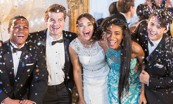 A group of happy teenagers in formal dresses and tuxedos celebrating prom night, representing CNS Limo's luxury Houston prom transportation.